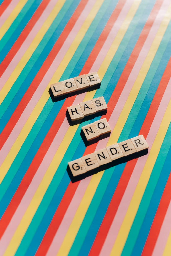 Scrabble tiles on a rainbow background spell 'Love Has No Gender', celebrating inclusivity.